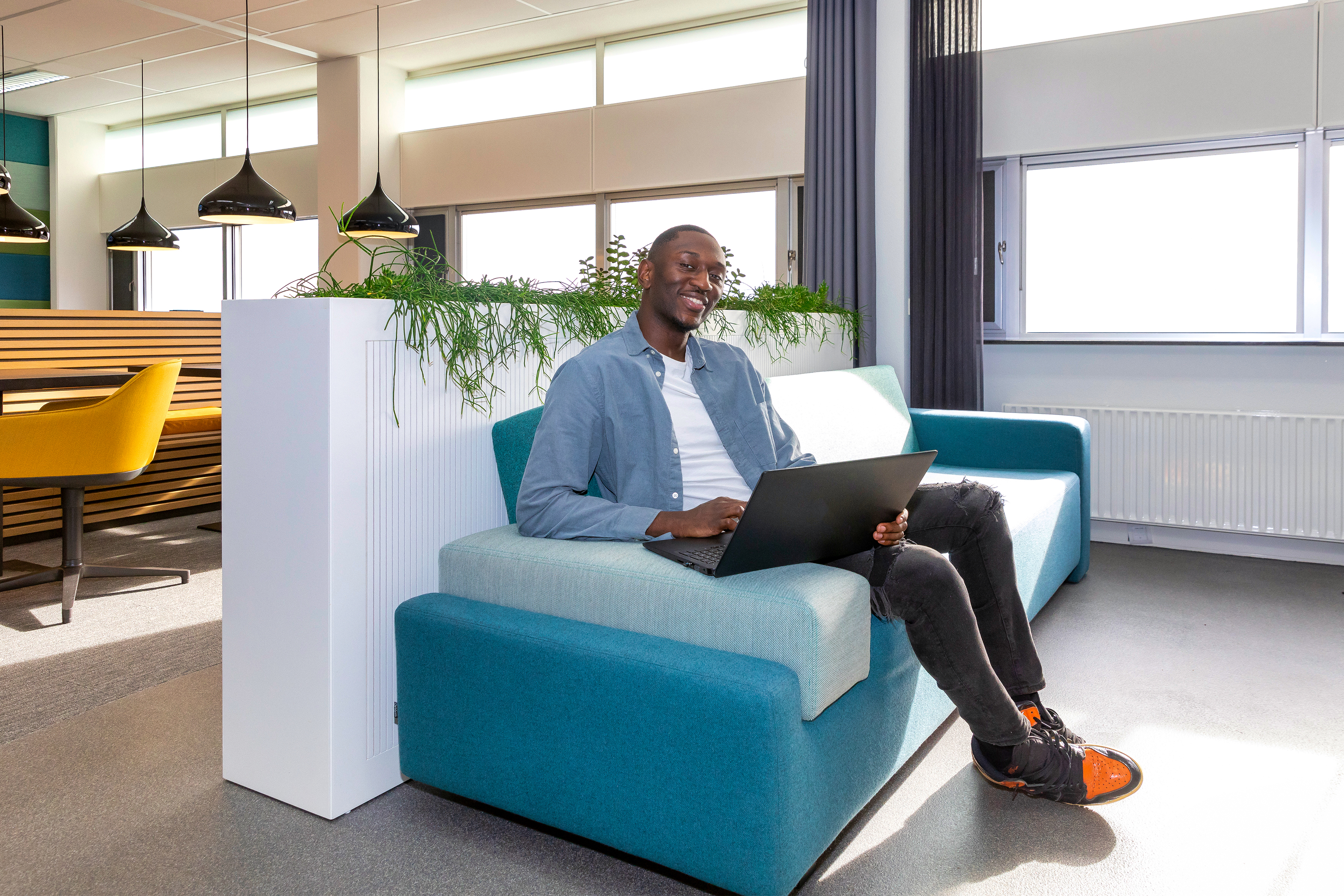 Medewerker van GBLT zit op kantoor op een bank met een laptop op schoot.