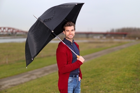 Man staat met paraplu op de dijk