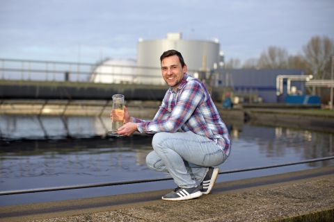 Afbeelding van hurkende man die maatbeker met water vasthoudt bij een waterzuiveringsinstallatie